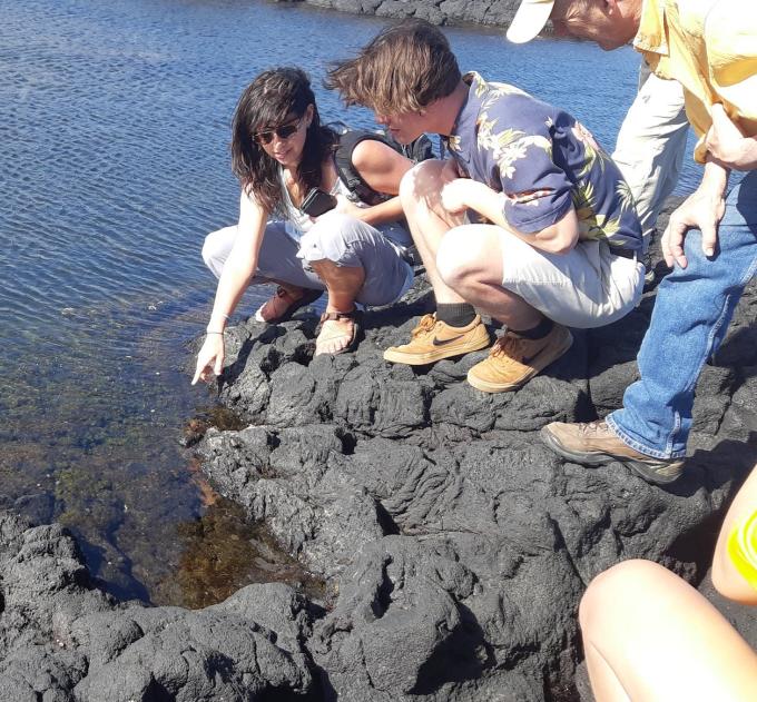 Three people stand on a rocky section above water.